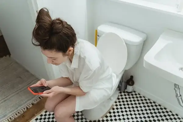 여성이 변기에 앉아 휴대폰을 하고있는 장면