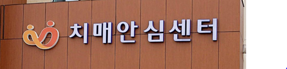 치매안심센터의 간판과 로고가 건물에 붙어 있는 모습. 주황색 8자모양 로고와 함께 하얀 글씨로 치매안심센터가 쓰여 있다.