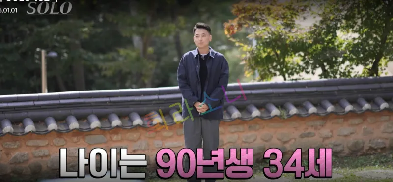짙은 파란색 재킷을 입은 24기 상철이 야외에서 서 있다. 그는 양손을 모으고 담담한 표정으로 카메라를 바라보고 있다. 화면 하단에는 