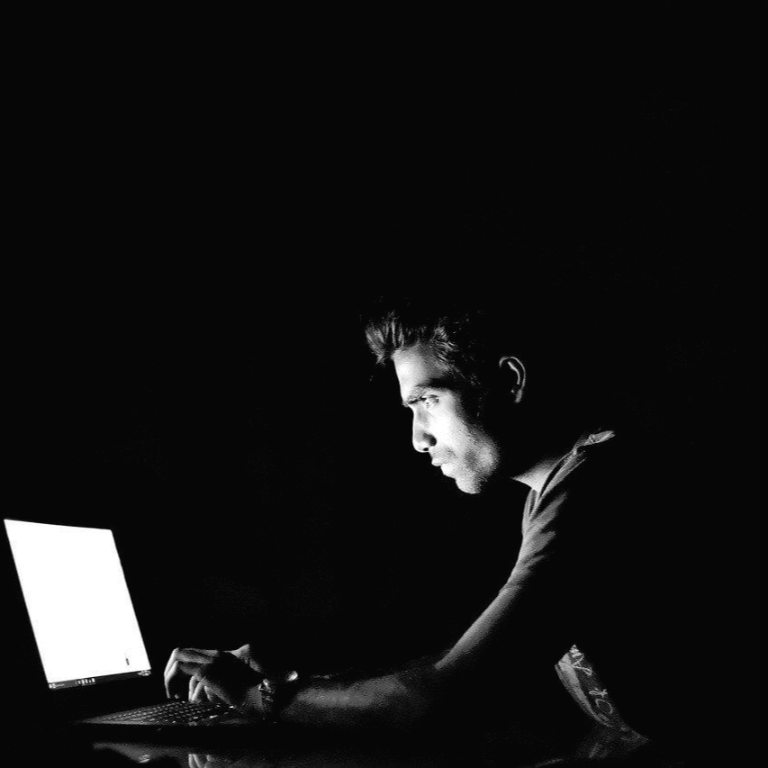 어두운 공간에서 노트북을 이용해서 글을 작성하고 있는 남자