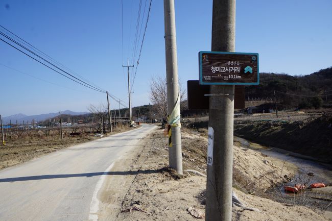 푸른 하늘&#44; 가운데 전봇대 2개&#44; 앞 전봇대에 붙은 이정표&#44; 남은 거리 10.1km&#44;