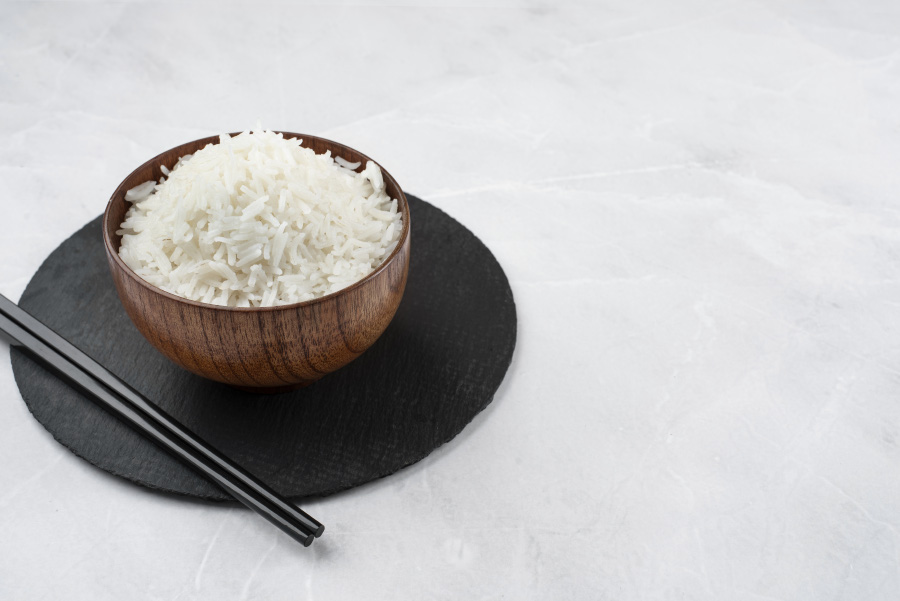 흰색 바닥 위에 동그랗고 검은 깔판을 놓고 그 위에 쌀밥을 한가득 담은 고동색 나무 그릇을 놓아두고 그 옆에 검은 젓가락을 놓고 찍은 사진
