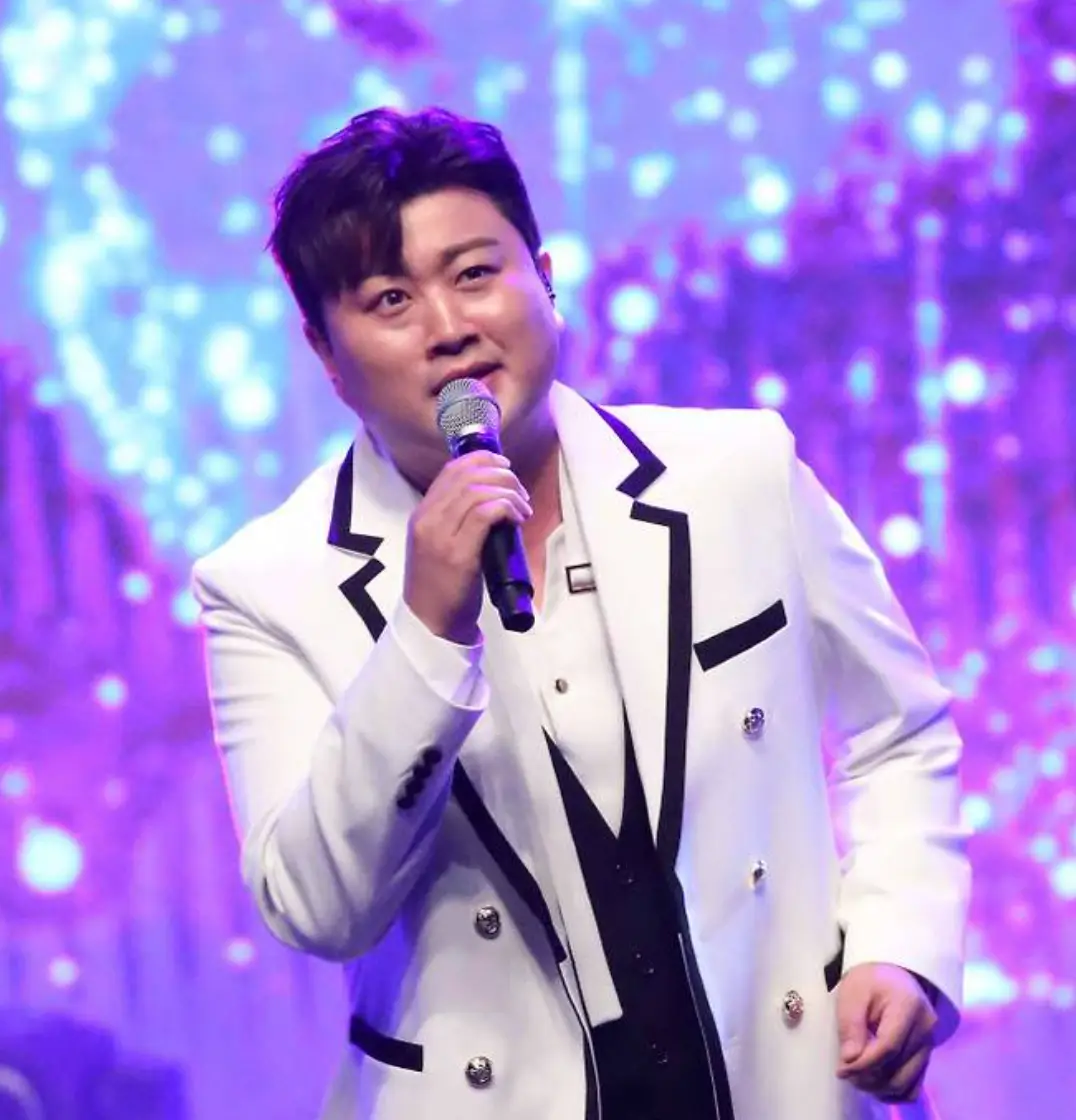 보라색 배경 흰 양복을 입은 김호중이 오른손에 마이크를 들고 노래하는 모습