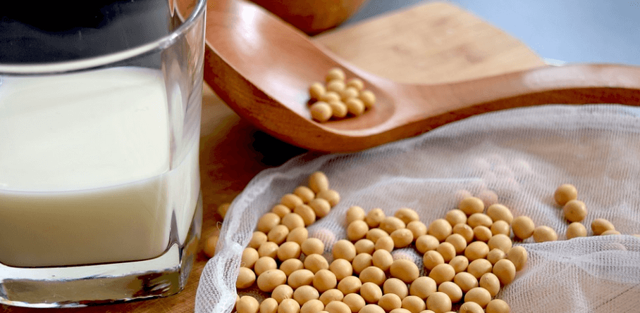 두유 한 컵과 여러 개의 콩이 놓여 있습니다.