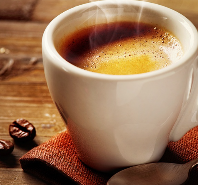 흰색 도자기 컵에 커피가 담겨져 있고 커피열로 인한 연기가 올라오고 있다.