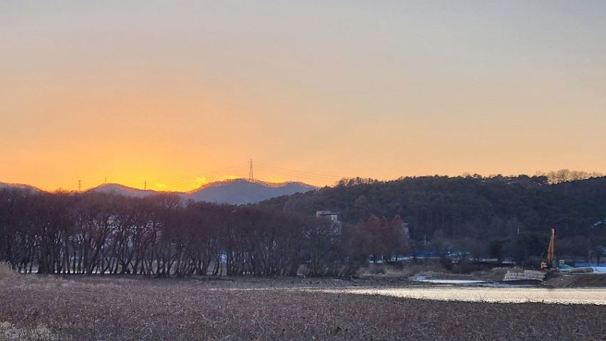 버드나무숲 뒤로 해 질 무렵, 하늘에 엷은 노을빛, 앞에는 호수바닥, 가운데 호수물, 멀리 야산, 그 위로 지나가는 고압선 철탑,