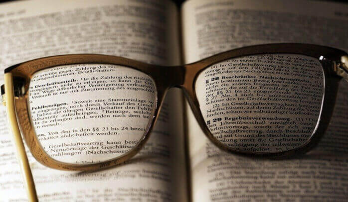 펼쳐진 책 위에 옅은 갈색의 뿔테 안경이 놓여있는 모습