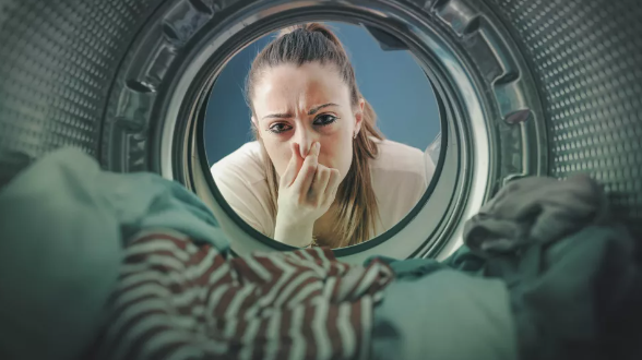 세탁기 안에서 빨래를 바라보며 코를 막고 있는 여성(이미지 출처: Shutterstock)
