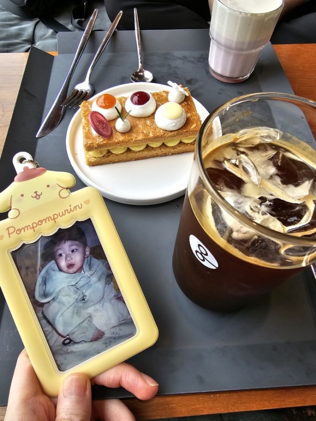 직장인 A씨가 카페에서 커피&#44; 케이크를 앞에 두고 찍은 &lsquo;예절샷&rsquo;. 포토카드에는 A씨가 좋아하는 배우 김강민의 어린시절 모습이 담겨있다. A씨 제공