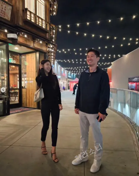 하림과 리키가 함께 멀찍이 떨어져 웃으며 찍은 사진. 하림은 남색 셔츠에 회색 조거 팬츠를 입었고 하림은 상의&#44; 하의 모두 올 블랙에 검은 색 힐을 신었다.
