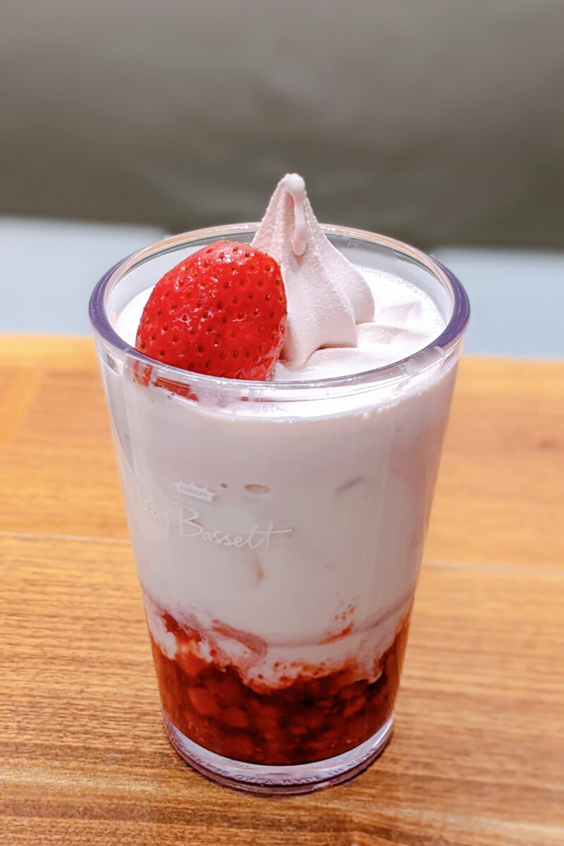 투명한 컵 안에 담긴 아이스크림 딸기 라떼 상단에 붉은 딸기가 장식되어 있는 모습