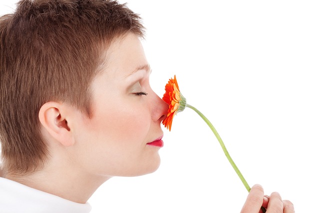 짧은 머리의 여자가 빨간 꽃을 코에 대고 향기를 맡고 있다.