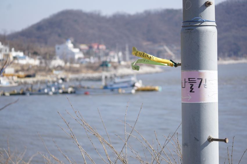 우측 회색 전봇대에 붙은 강화나들길 스티커, 뒤로 아웃포커싱 된 건평항 풍경,