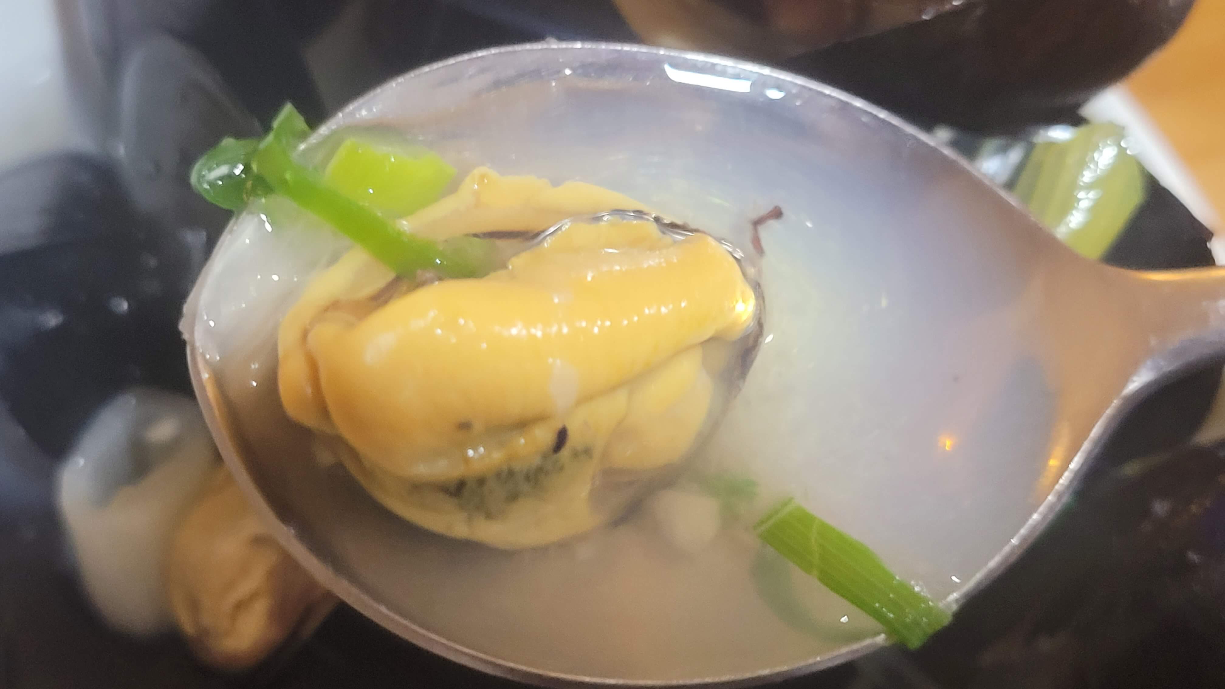한국식으로 조리된 홍합 한 조각, 파와 함께 스푼에 담겨진 모습