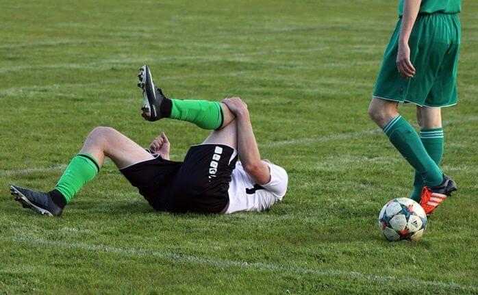 축구를 하던 남성이 무릎을 감싸쥔 채 잔디밭에서 뒹굴고 있는 모습 