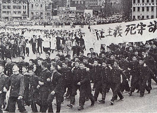 흑백 사진속에 학생들이 현수막으들고 시위에 나서고있다.
