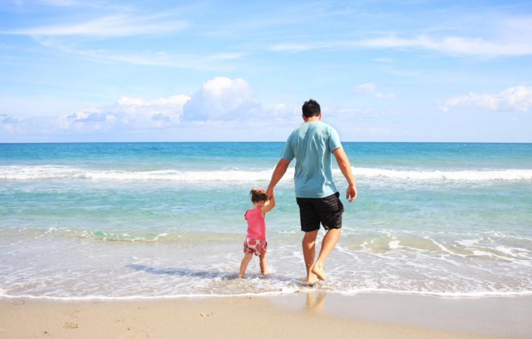 해변에서 아빠와 딸이 손을 잡고 놀고 있다.