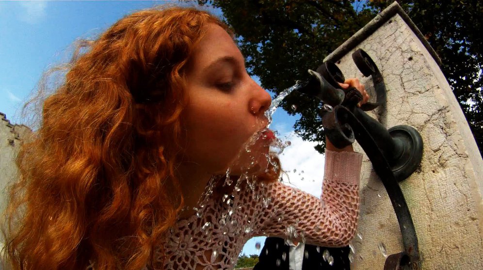 한 여성이 거리에 있는 식수대에 얼굴을 가까이 대고 물을 먹고 있는 장면