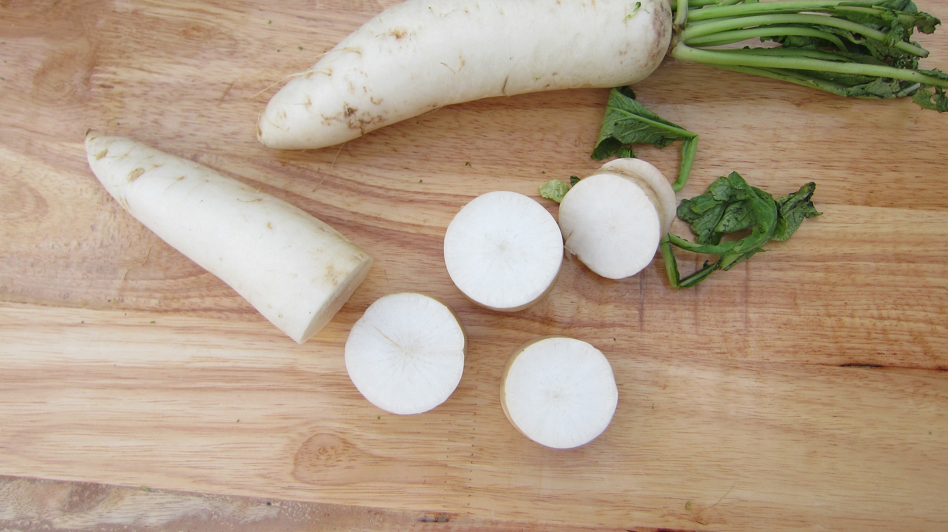 white-radish-2934281_1920 나무로 된 테이블 위에 커다란 무를 2개 놓고, 1개는 통무를 그대로 두고, 하나는 통무를 반으로 잘라서 머리 부분은 또 토막을 내 놓은 사진