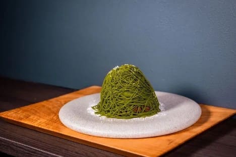녹색의 몽블랑 디저트가 도자기 같은 회색 접시 위에 올라가 있다.