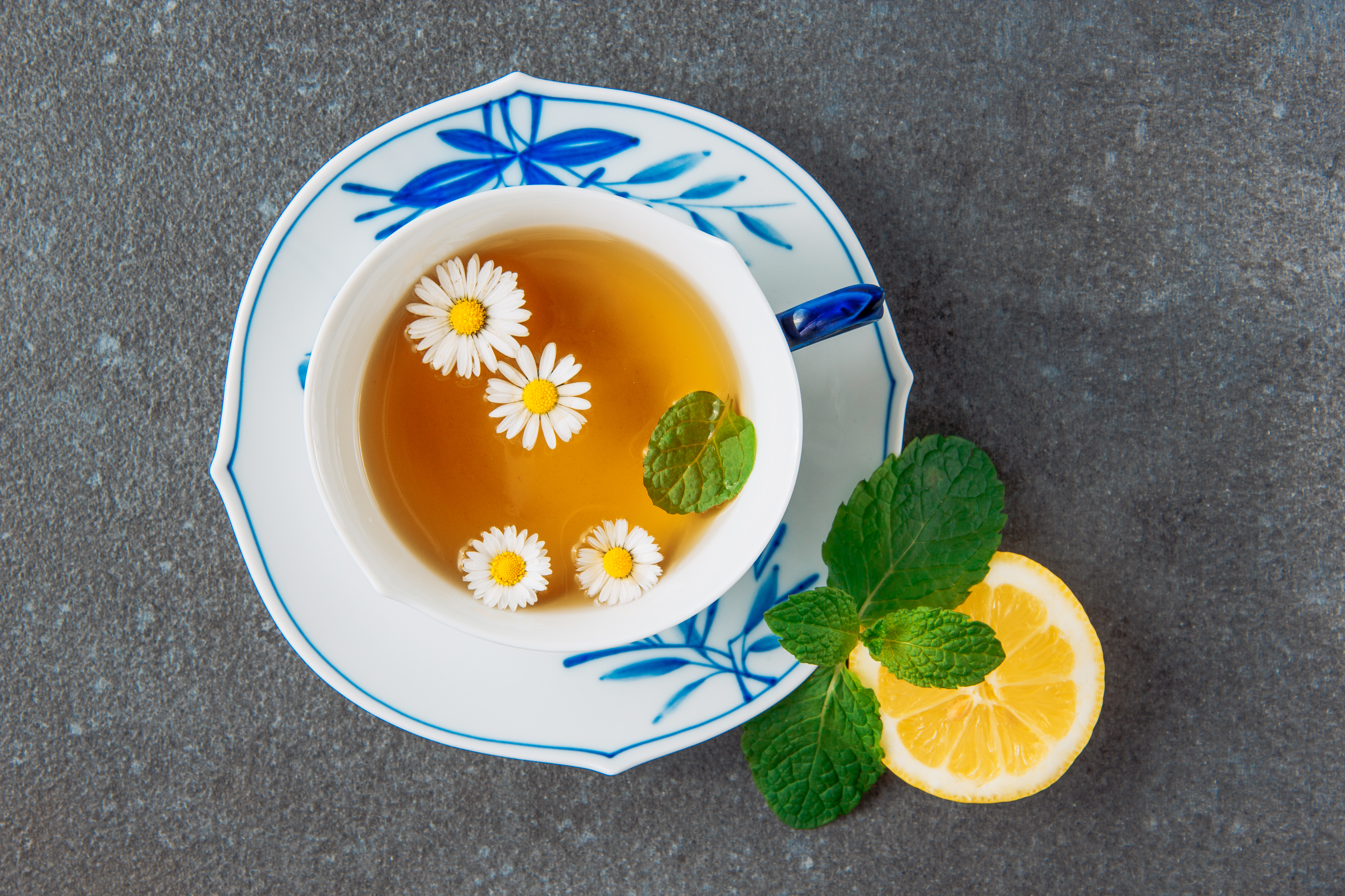 brewed-chamomile-tea-with-half-lemon-green-leaves-cup-saucer-grey-stucco-background-top-view