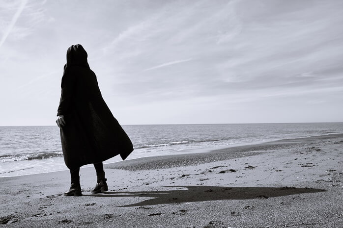 바다를 향해 서있는 긴코트를 입은 여자의 흑백사진