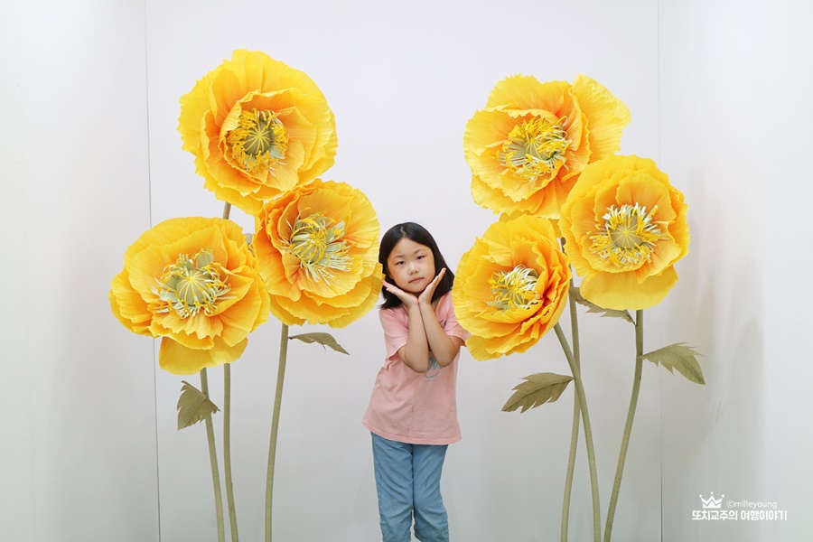 노란색 종이 꽃 모양 가운데 손 꽃받침을 하고 사진을 찍고 있는 아이