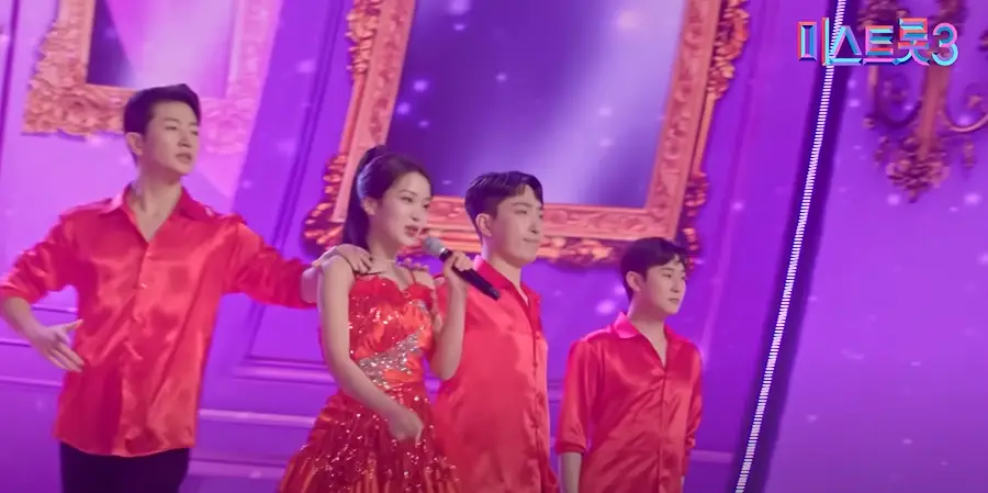 미스트롯3- 보라색 무대 빨간 와이셔츠를 입은 백댄서사이들에서 빨간 옷을 입고 왼손으로 마이크를 든채 걸어가면서 노래하는 김소연
