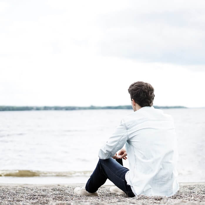 흰 셔츠에 청바지 입은 남자가 앉아서 호수를 바라보고 있는 모습