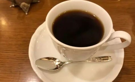 흰색 접시위에 커피와 티스푼이 올려져 있다.