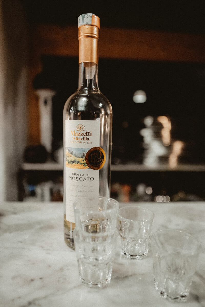 모스카토 다스티 와인병이 흰 탁자 위에 놓여있고 병 앞에는 유리잔 몇 개가 놓여있다.