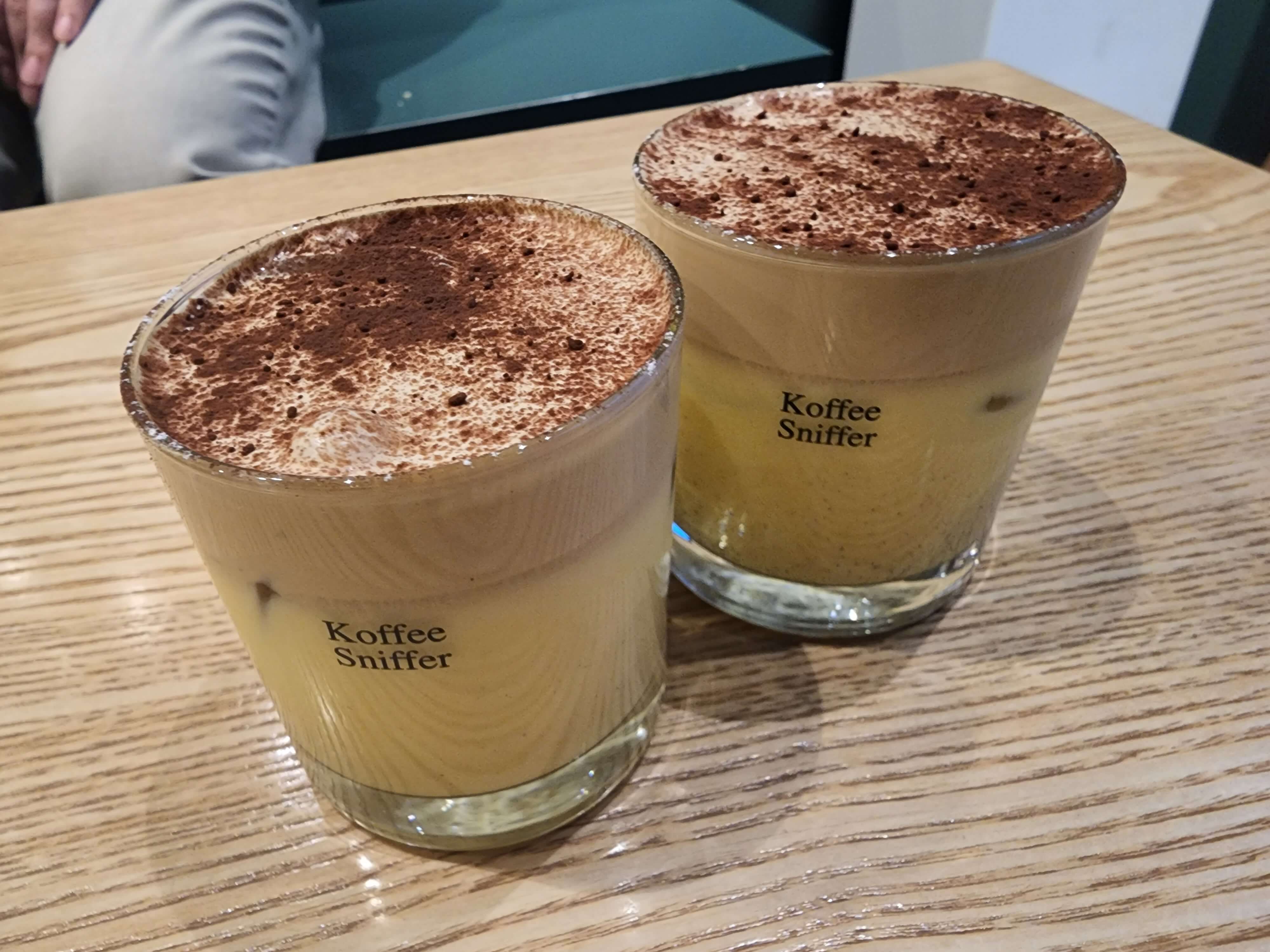 짧고 동그란 유리잔에 koffee Sniffer라고 검정색 글씨로 프린팅되어 있다. 노르스름한 커스터드 크림 위에 연갈색 에스프레소 크림이 층을 이루고 있고 그 위에 코코아 파우더가 잔뜩 뿌려져 있다.