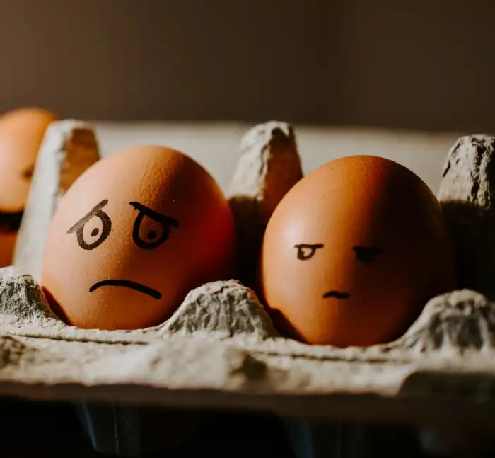표정이 그려진 계란 두 개가 계란판에 올려져 있고&#44; 왼쪽의 계란은 오른쪽을 째려보는 표정을 짓고 있고&#44; 오른쪽 계란은 옆 계란의 눈치보는 얼굴을 하고 있다