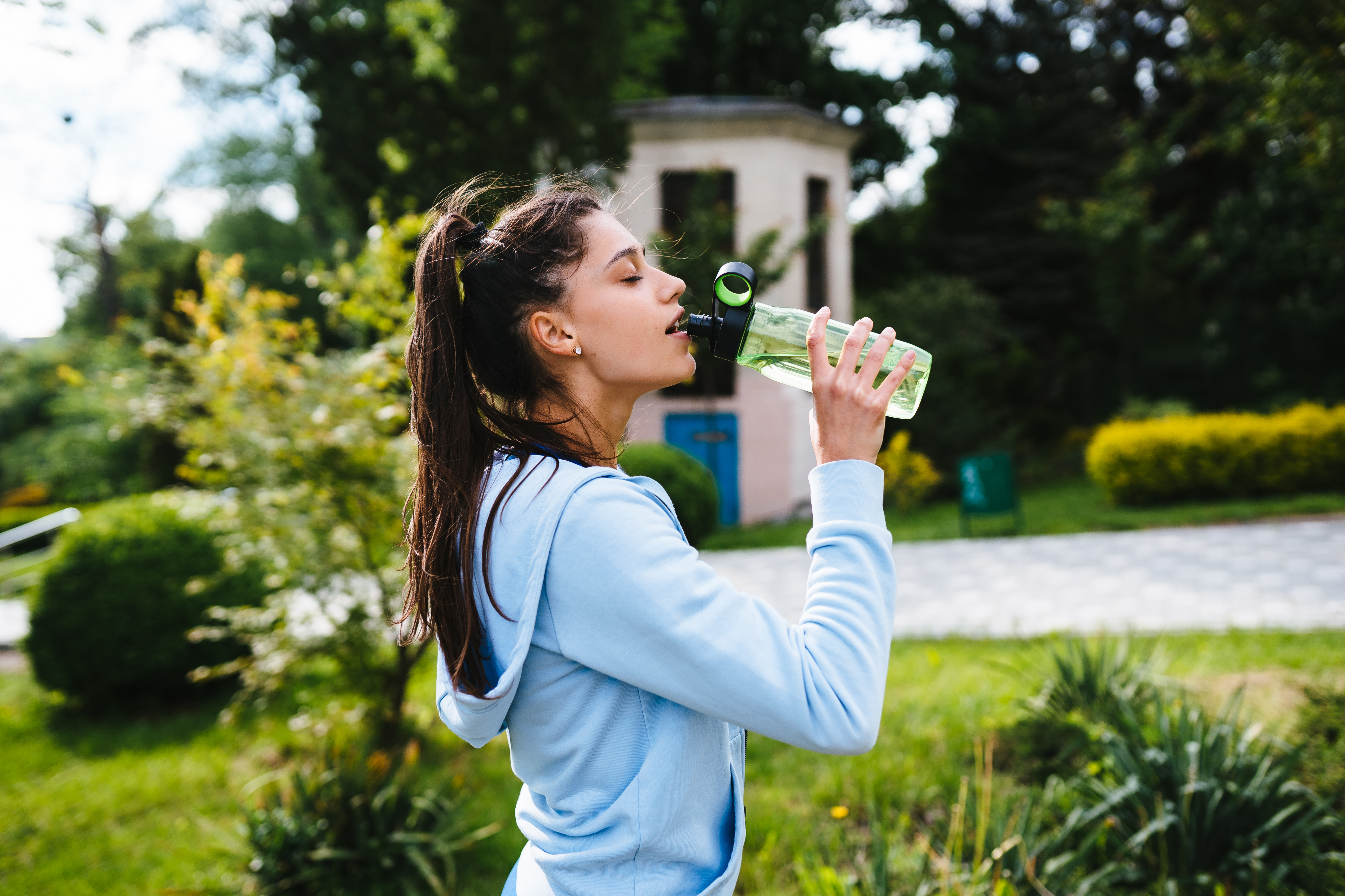 young-woman-sporting-suit-drinks-water-from-bottle-after-outdoor-gymnastics-summer
