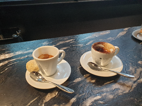 테이블 위에 에스프레소 잔 두 개가 놓여있다. 에스프레소(왼쪽)에는 인절미 쿠키도 놓여있다.