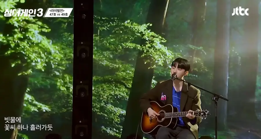 싱어게인3 - 검은색 자켓에 파란 가로줄무늬 티를 입고 갈색기타를 치며 의자에 앉아 스탠딩 마이크앞에서 노래부르는 49호