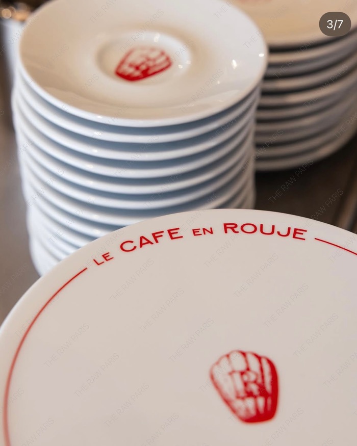 ⁠A stack of white porcelain plates with red borders and red madeleine logos printed with Le Cafe en Rouje⁠
