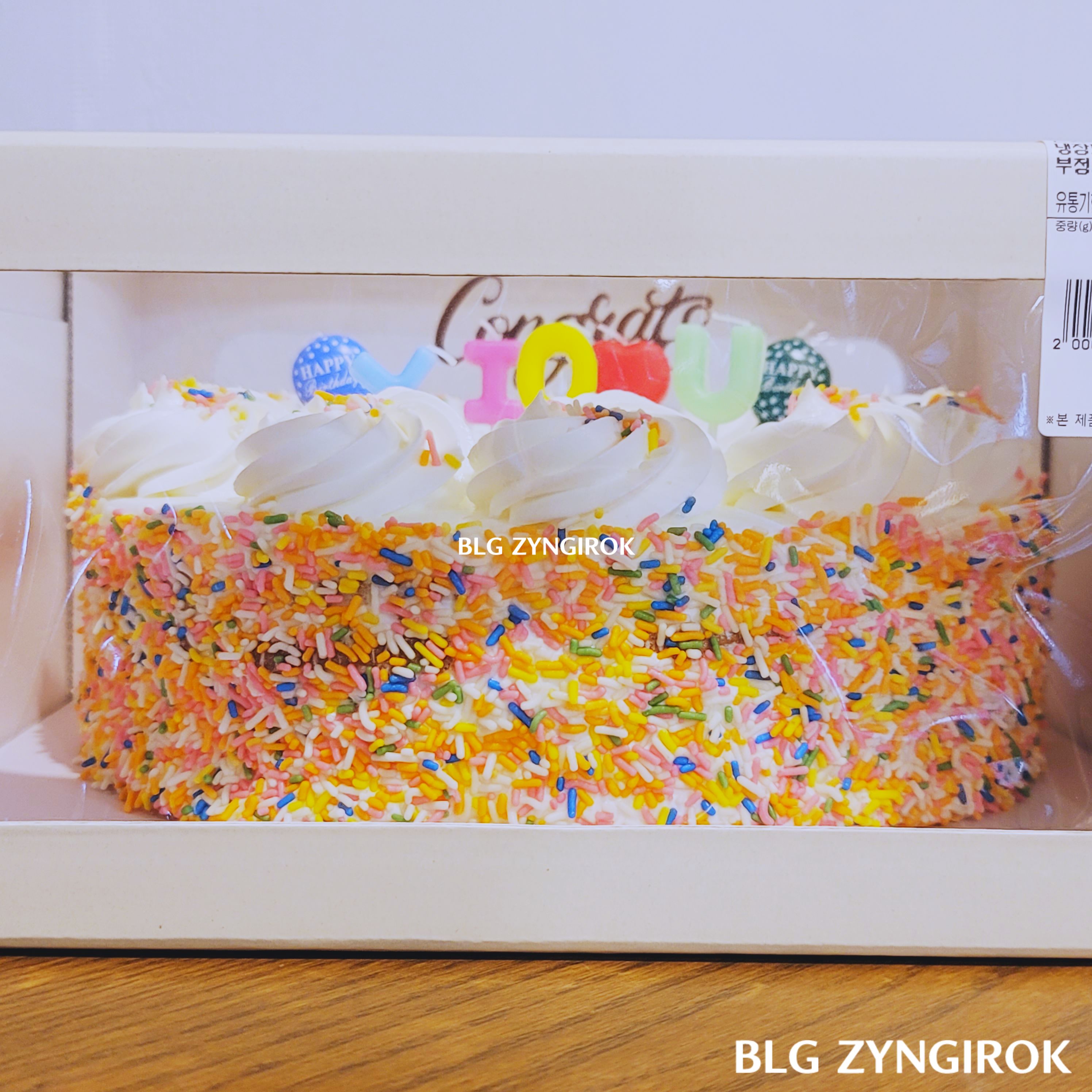 코스트코-케익-옆면-모습이다.-생크림-케익에-형형색색-설탕-장식들이-붙어있다.