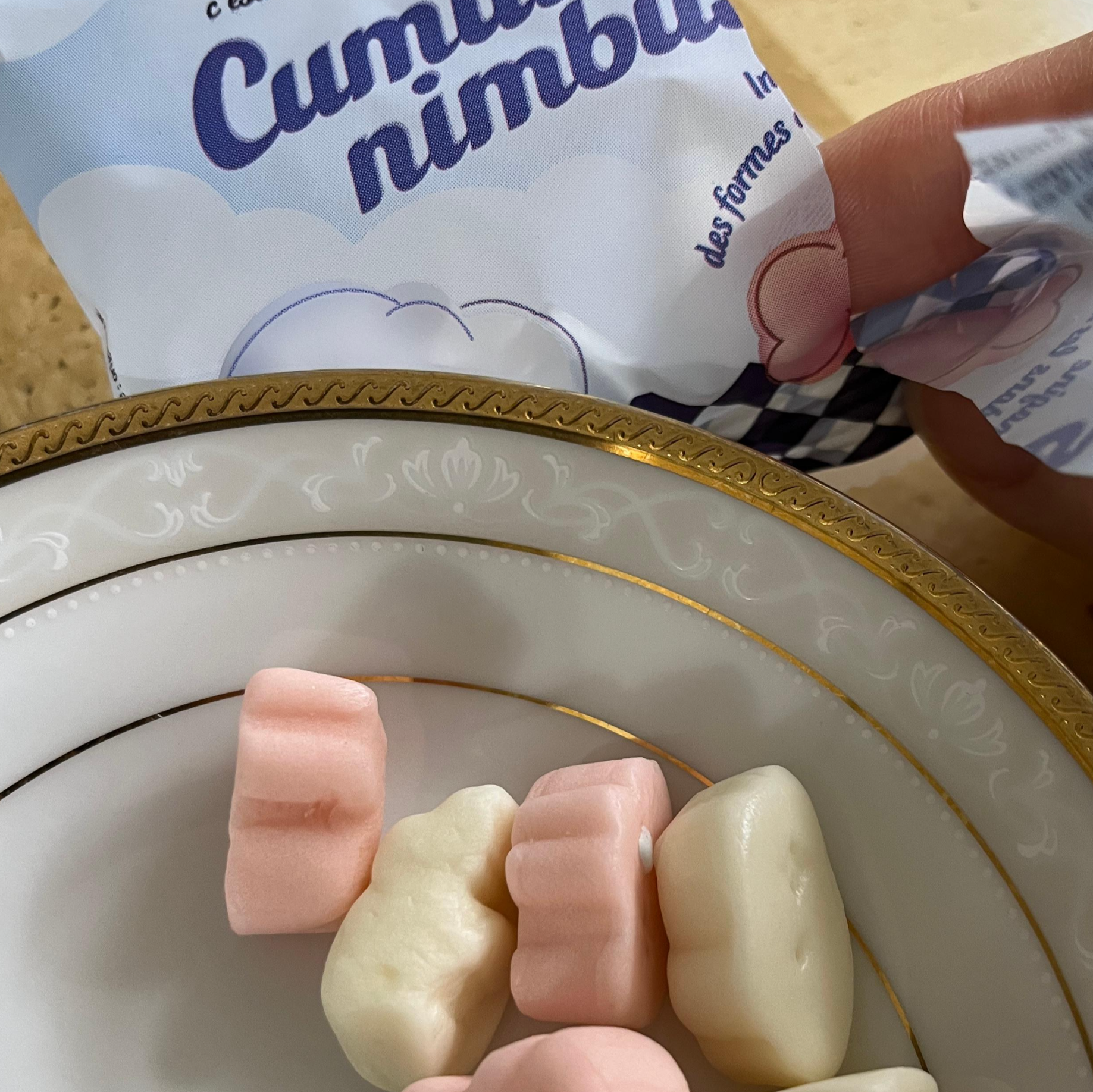 스카이블루 색상의 '큐물로 님부스(Cumulo nimbus)' 파우치를 개봉하여 마시멜로 질감의 구름 모양 젤리들을 하얀 접시에 담아낸 모습. 석유계 색소 없이 천연 원료로만 색을 낸 뽀얗고 부드러운 핑크색, 흰색, 하늘색의 뭉게구름 모양 젤리들이 찰진 텍스처를 드러내고 있다.