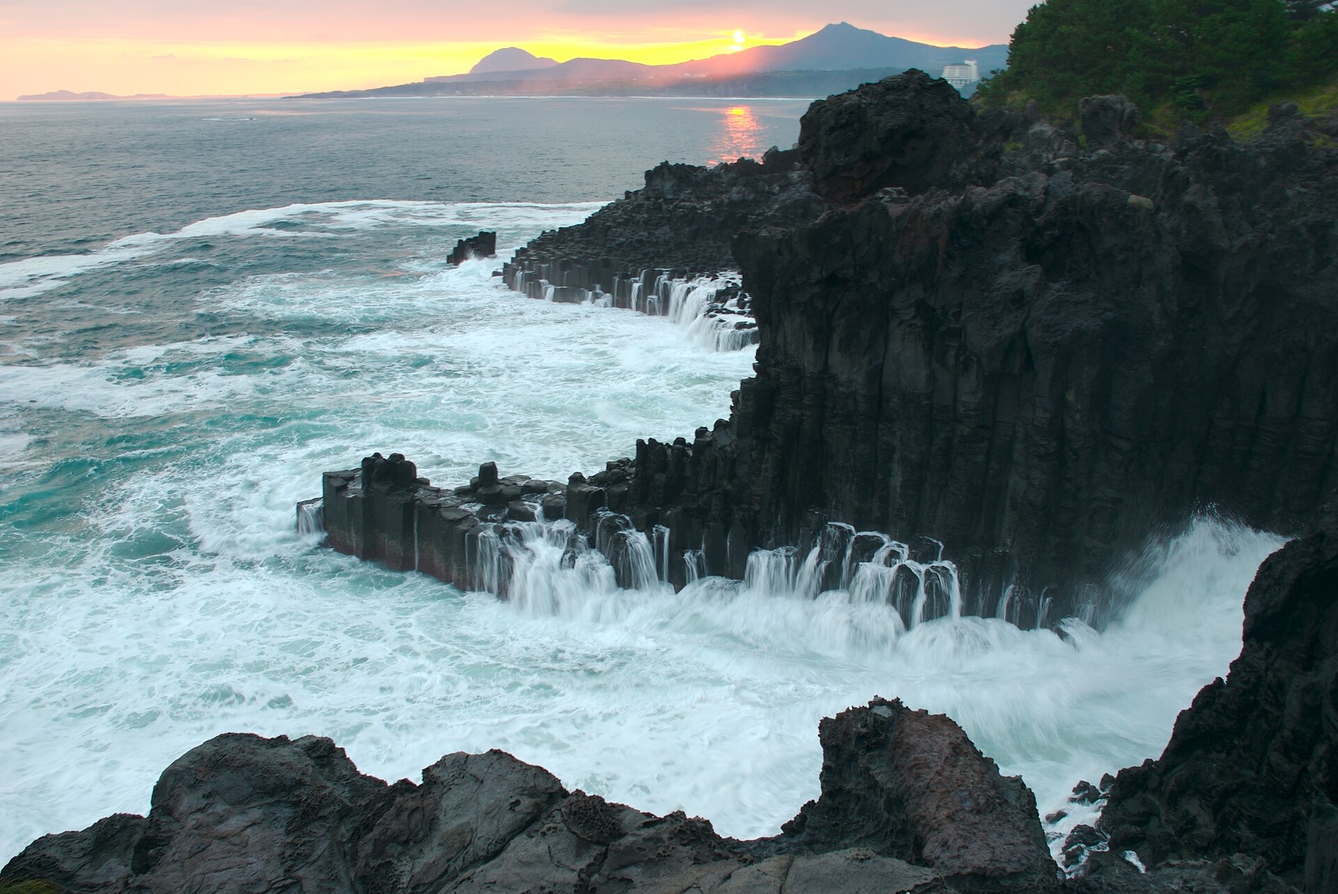 Rough waves breaking over the columns of Jusangjeolli Cliff at sunset
