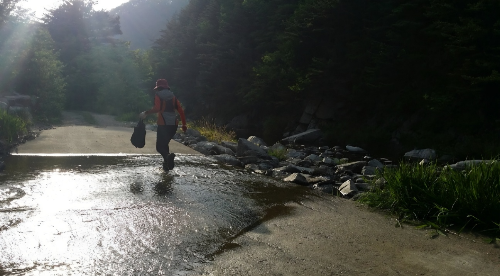 붉은 모자를 쓴 60대 여성이 선달산 산행 중 시원한 계곡 물길을 가로질러 건너가는 뒷모습