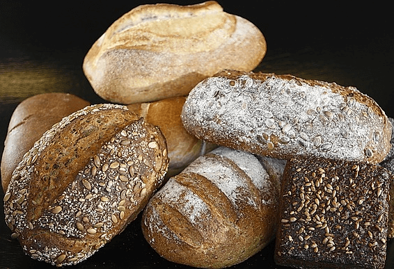 타원형의 통밀빵 7개가 한군데 모여있다. 표면은 거칠어보이고, 씨앗이 박힌 빵도 있다.