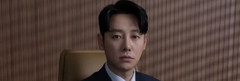 재판석을 배경으로 정장을 입은 채 무심한 표정으로 앉아 있는 한무영