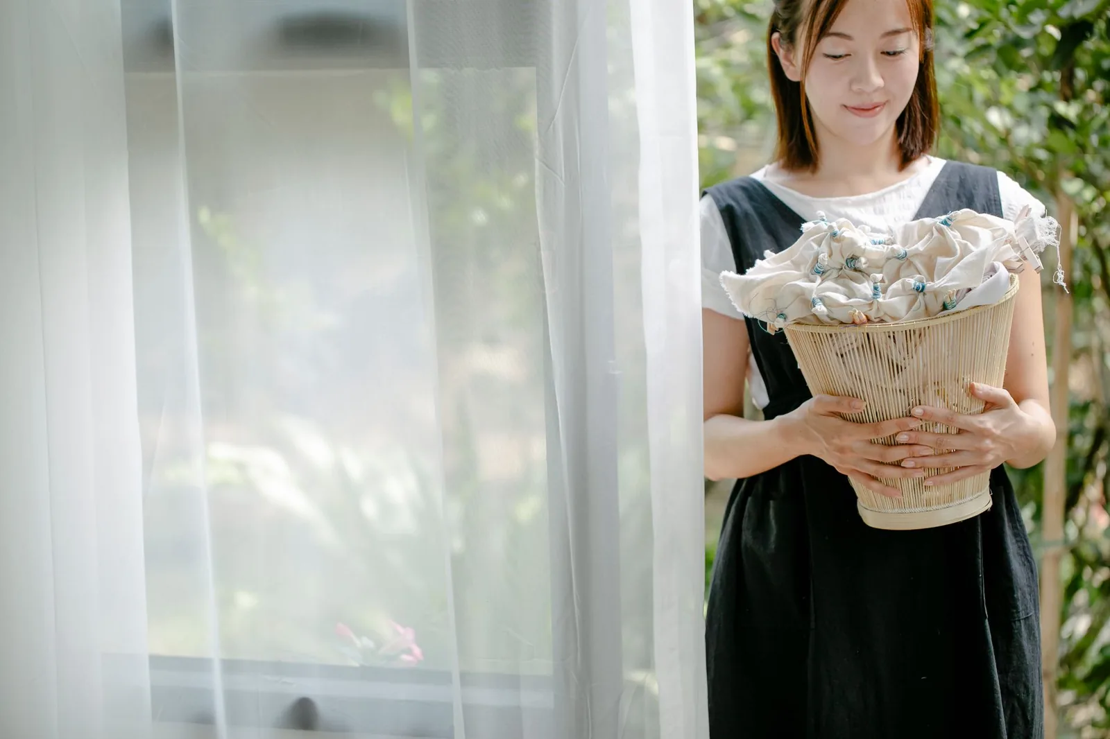 화창한 정원에서 수제 직물을 담고 있는 바구니를 들고 있는 쾌활한 젊은 여성, 자연스러운 공예를 구현합니다.
