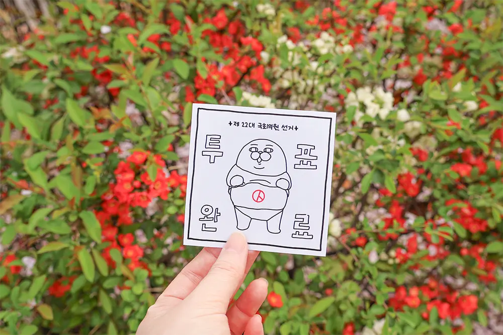 알록달록한-다양한-꽃-배경으로-투표-인증-종이-들고-있는-손