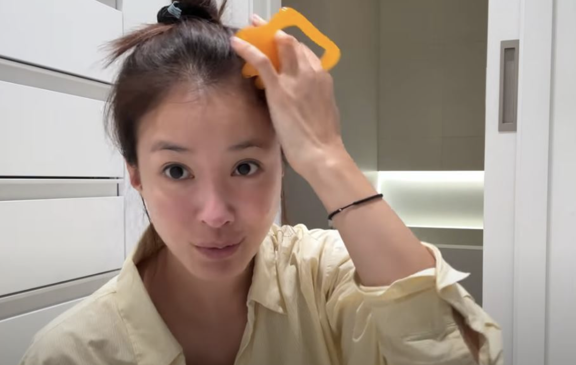 머리를 묶은 여성이 노란 괄사 도구로 이마 근처 두피 마사지를 하고 있다.