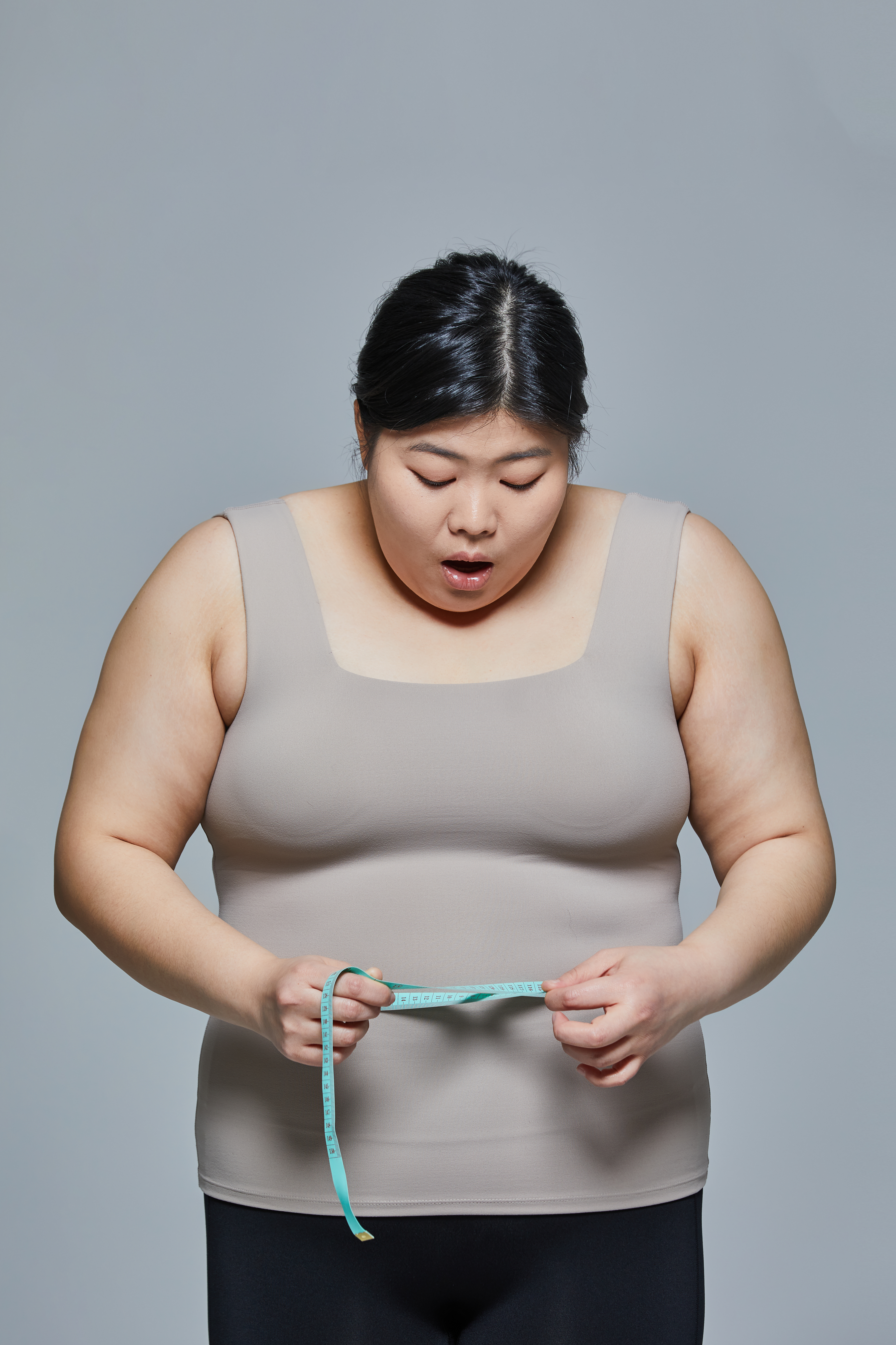 뚱뚱한 여성이 줄자로 배둘레를 확인하며 놀라는 사진