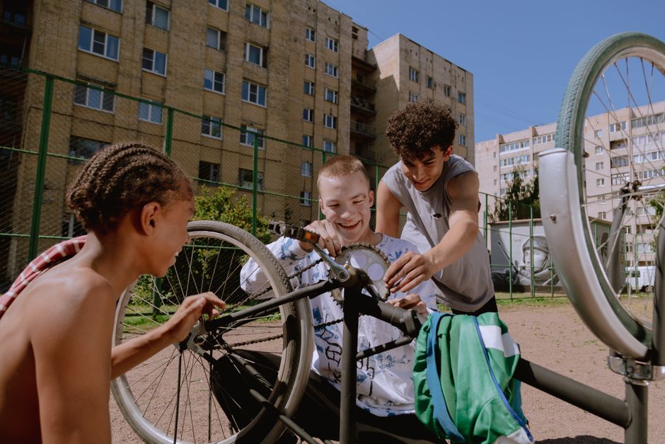 Three teenagers happily fixing a bicycle together outdoors on a sunny day, showcasing teamwork.