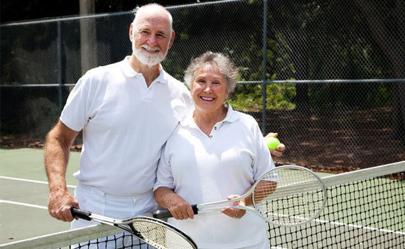 노년기 부부가 테니스장에서 카메라를 보고 웃고 있음