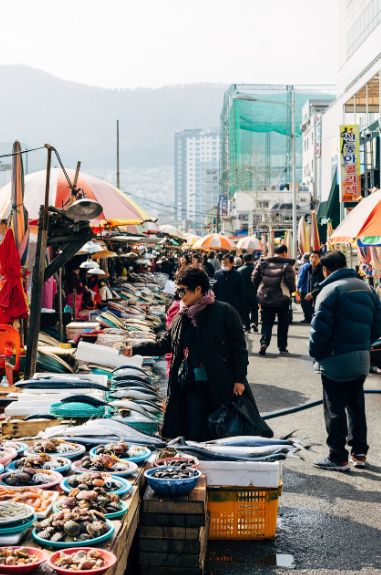 사람들이 북적이는 한국의 재래시장 에서 해산물을 구경하고 있는 모습. 다양한 해산물과 활기찬 시장 거리.